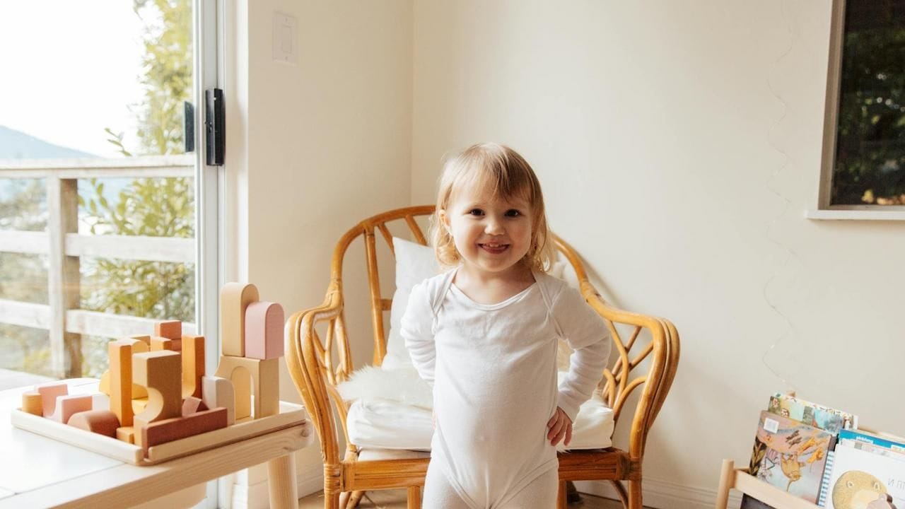 A young child standing near a washing machine that is running.